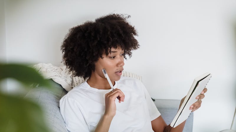 Focused young woman studying at home with a laptop and notepad, sitting comfortably on a couch.